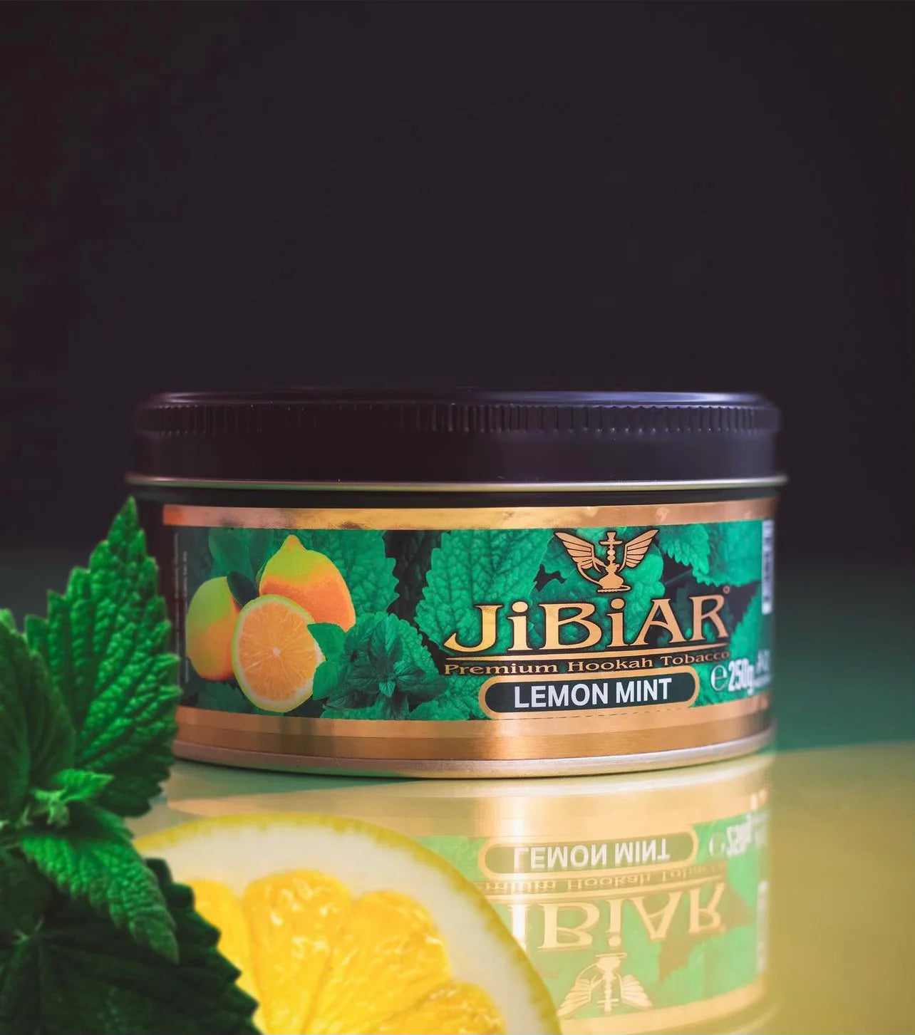 Jibiar Lemon Mint tobacco tin with green leaves and lemon slices on a reflective surface.